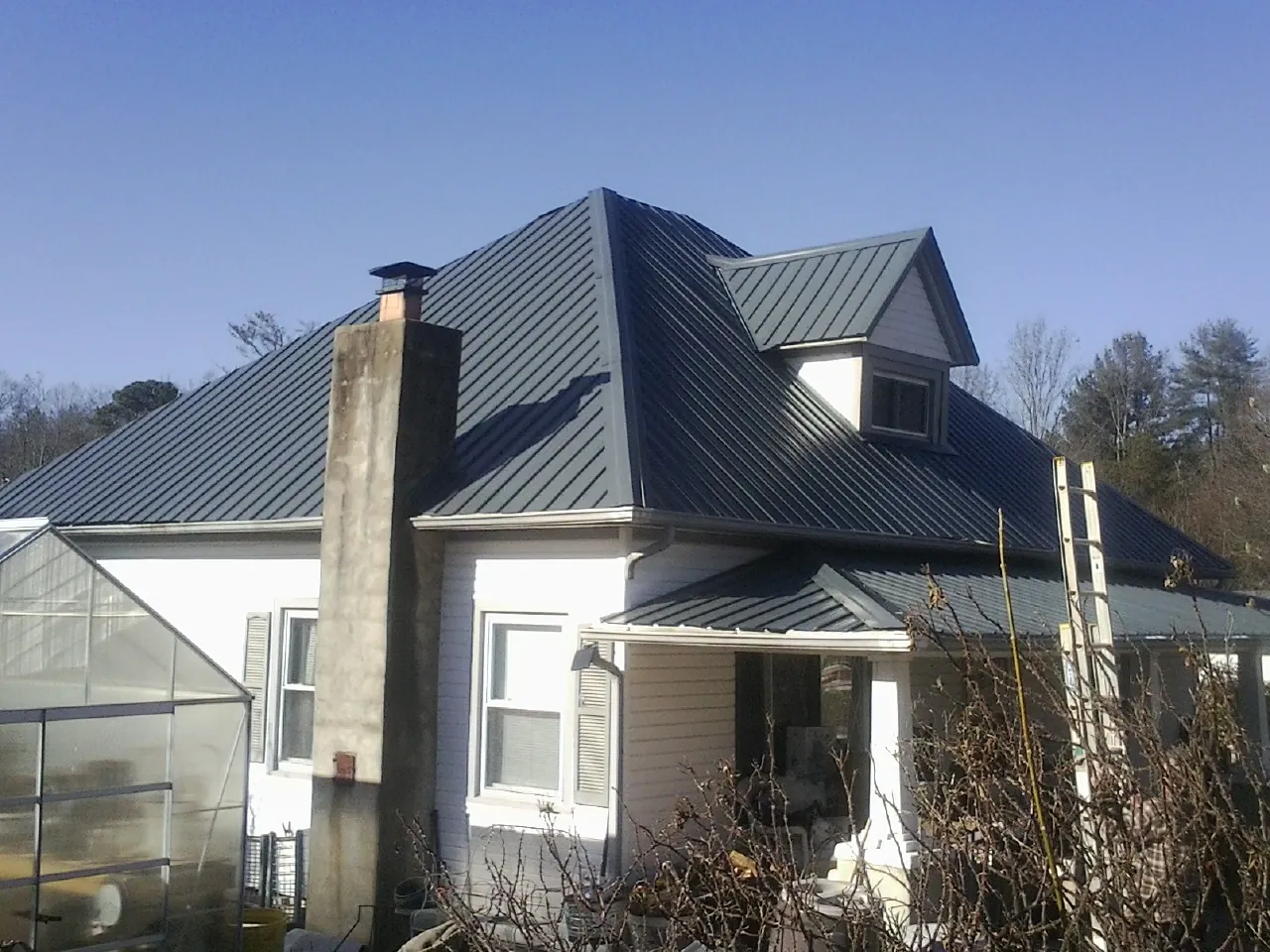 Dark blue standing seam metal roof on a white farmhouse with dormer — Slate & Tile Roof Repair by Roofing Brothers in Granite Canon