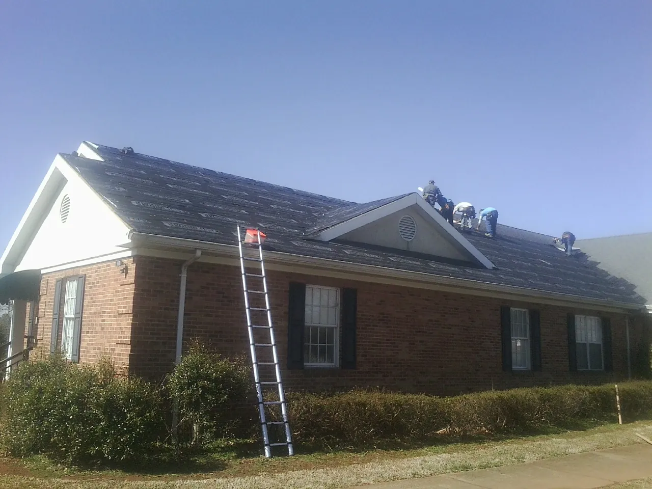 Crew tearing shingles off a brick ranch roof with a ladder set — Metal Roof Repair work by our crew in Granite Canon