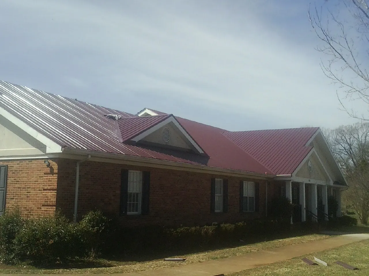 Red metal roof with gabled entries on a long brick building, from a Hail Damage Roof Repair job in Granite Canon