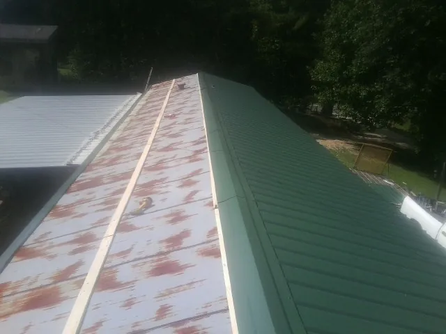 Old rusted panels beside newly installed green metal roofing — Wind Damage Roof Repair by Roofing Brothers in Granite Canon