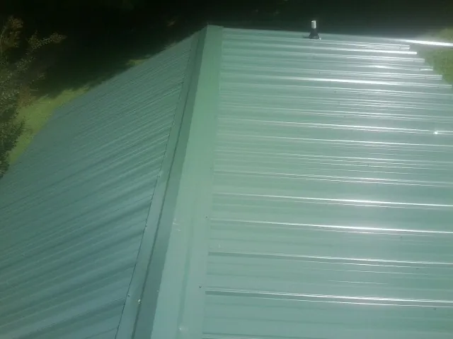 New green metal panels meeting at the ridge of a roof — Flat Roof Repair work by our crew in Granite Canon