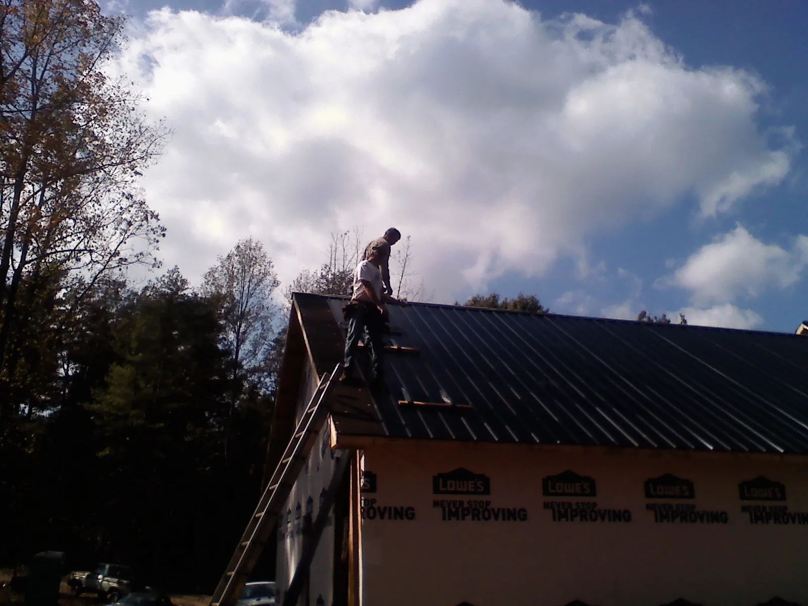 Roofer fastening dark metal panels high against a cloudy sky, from a Roof Inspection job in Granite Canon