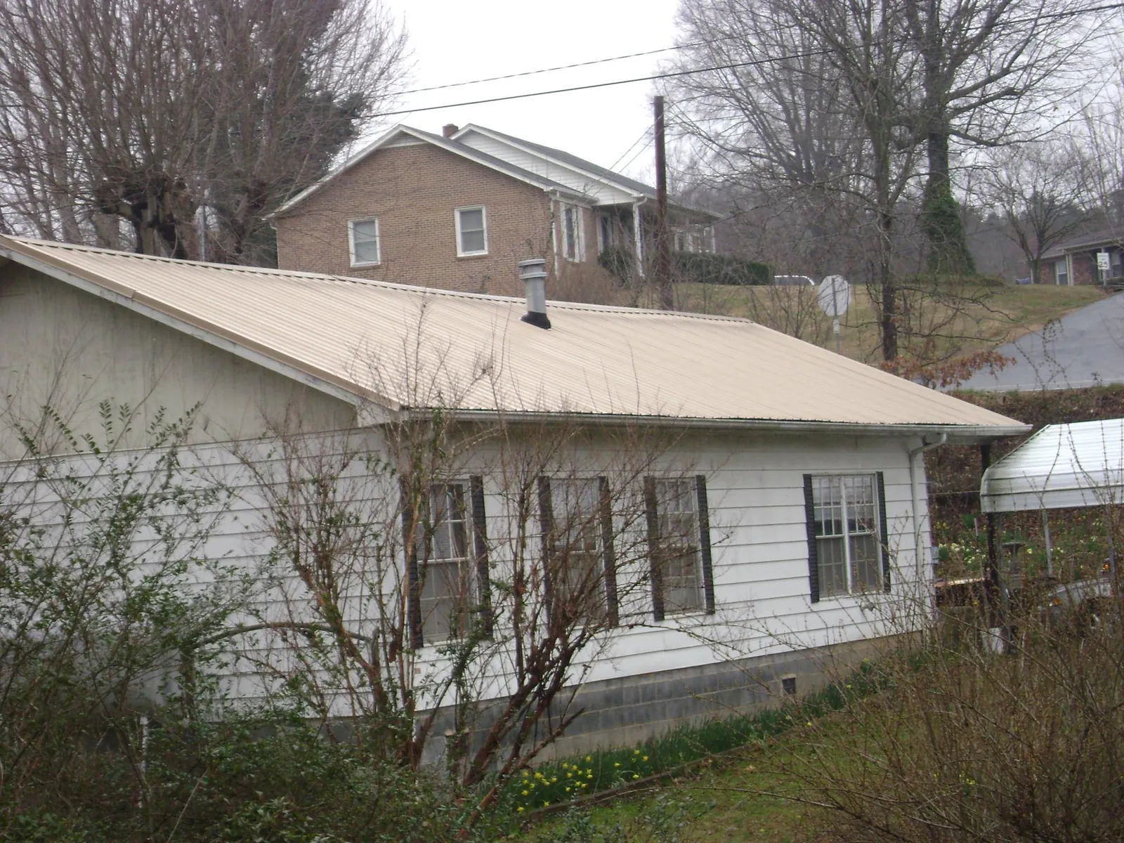Tan metal roof on a white sided house set into a hillside — Commercial Roofing by Roofing Brothers in Granite Canon