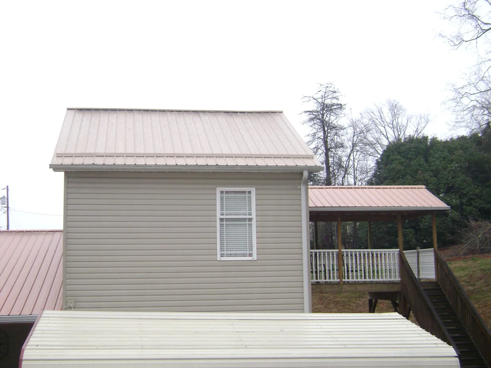 Tan metal roofs on a two story addition and attached porch, from a Roof Replacement job in Granite Canon